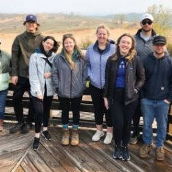 A group of people standing on a wooden platform with hills in the background.